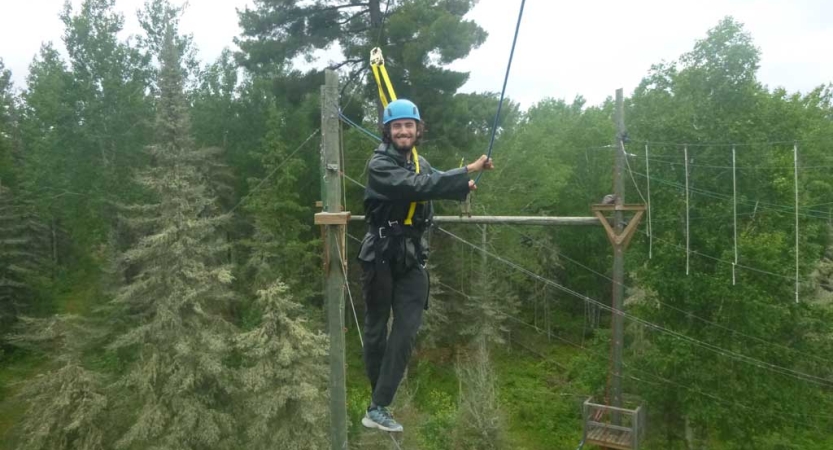 A person wearing safety gear is secured by ropes as they navigate a high ropes course. 